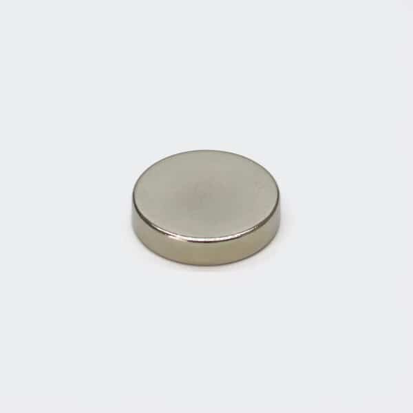 A nickel plated disc-shaped strong magnet laid flat on white desktop, with slightly rounded corners.