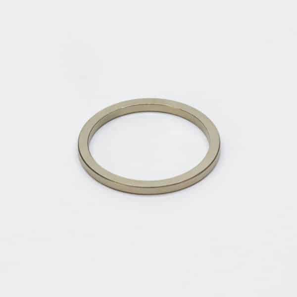 A nickel plated ring-shaped rare earth magnet laid flat on a white desktop, with chamfered edges.