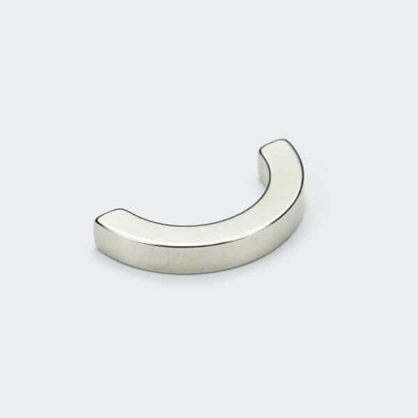 A silver nickel plated NdFeB magnet in the shape of half a ring, laid on a white desktop.