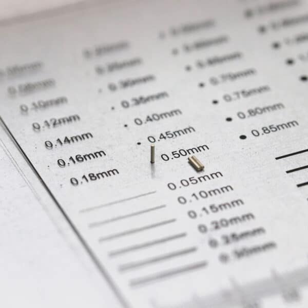 Three nickel plated tiny cylindrical NdFeB magnets diameter 0.5mm placed on a size estimation chart.