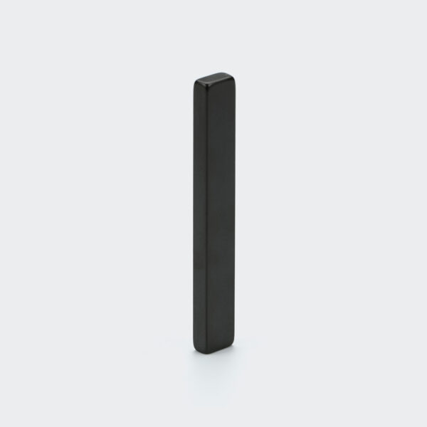 A black epoxy coated long thin neodymium bar magnet made from material grade H 120°C vertically standing on a desk