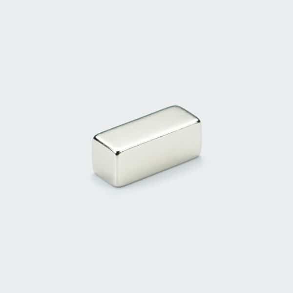 A smooth nickel plated square neodymium block magnet laid on a white desk top