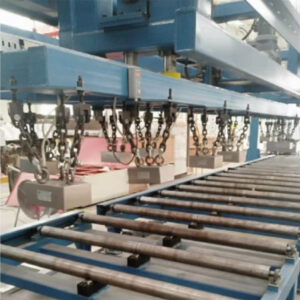 Electronically controlled magnetic lifting chucks suspended by chains from a blue overhead gantry, lifting steel billets off a roller conveyor in an industrial material handling system.